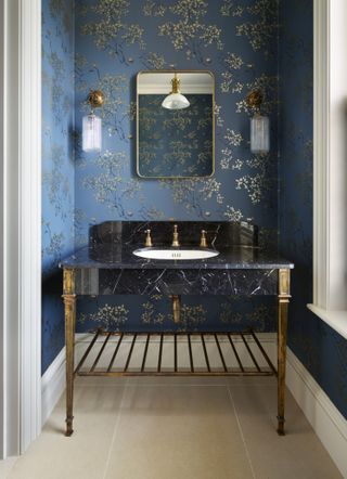 powder room with blue wallpaper, stone floor, marble/gold vanity unit