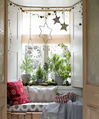 Christmas window decor ideas with star decorations hanging above a window seat with red cushions and Scandi blankets
