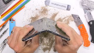 A screenshot of JerryRigEverything's Google Pixel Fold durability test, showing the phone folded backwards, breaking around the antenna line