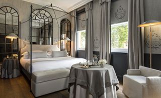 Bedroom in grey tones with a hardwood floor, four-poster bed and window-shaped mirrors