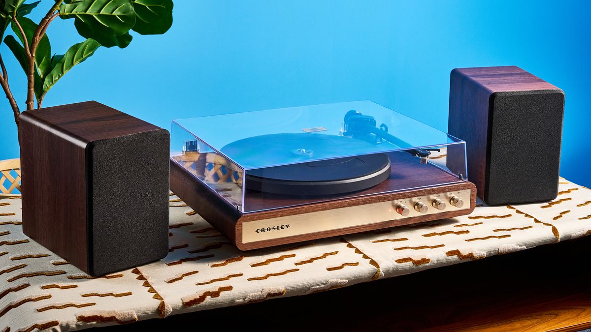 Crosley C65 turntable and bookshelf speakers photographed in front of a blue background on a brown table.