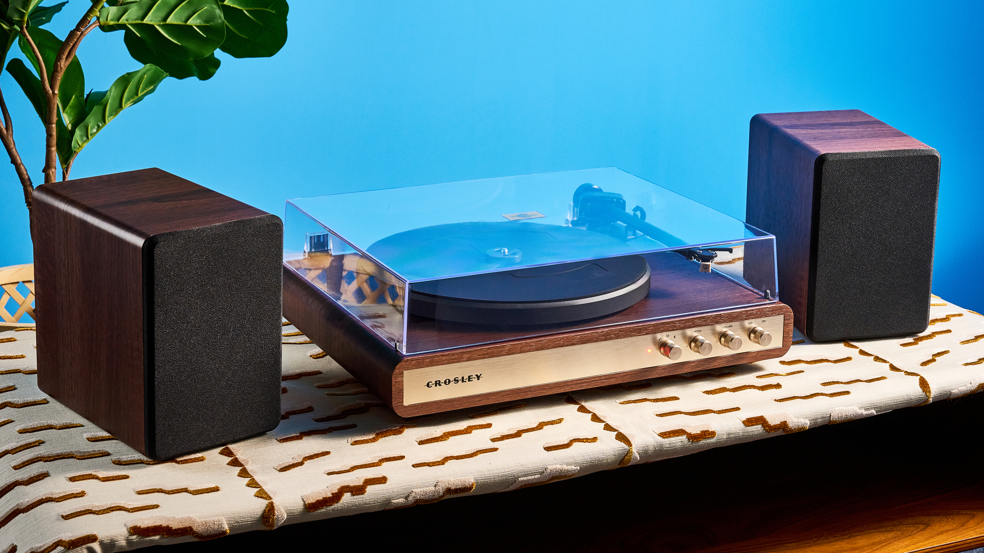 Crosley C65 turntable and bookshelf speakers photographed in front of a blue background on a brown table.