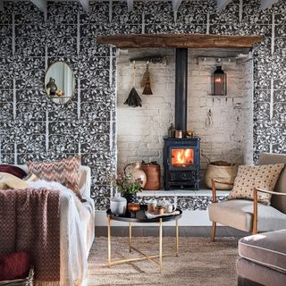 Rustic living room with patterned wallpaper and stove in inglenook fireplace