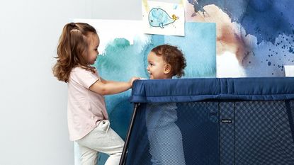 Two toddlers playing in a blue travel cot – one of the best travel cots you can buy