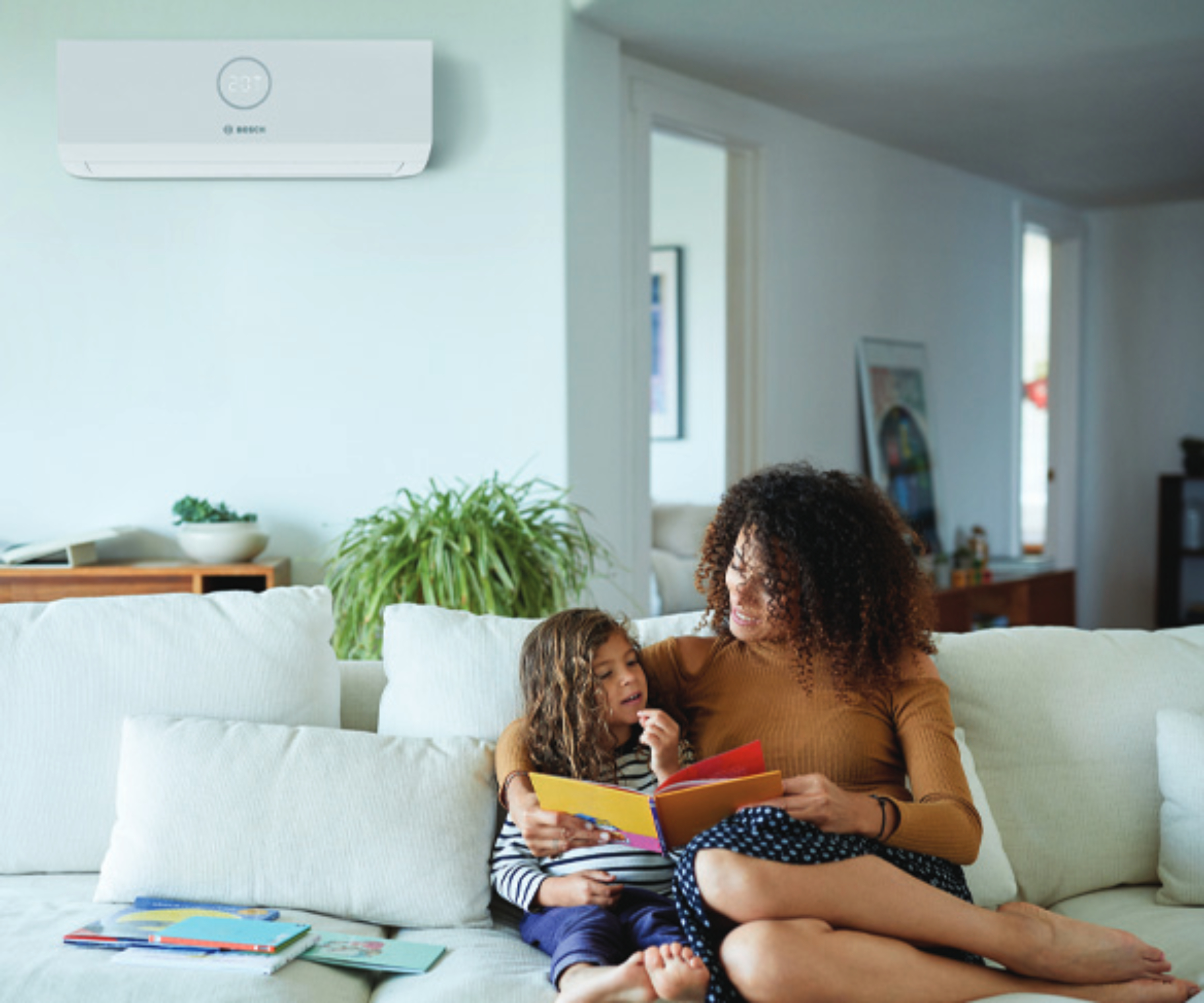 female adult and child sat on sofa reading book with air con unit on wall behind them