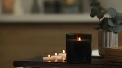 lit scented candle in black glass vessel in room