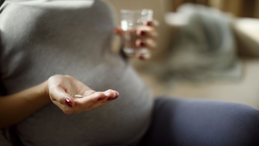 Closeup on belly of pregnant woman, who is holding a pill and water glass