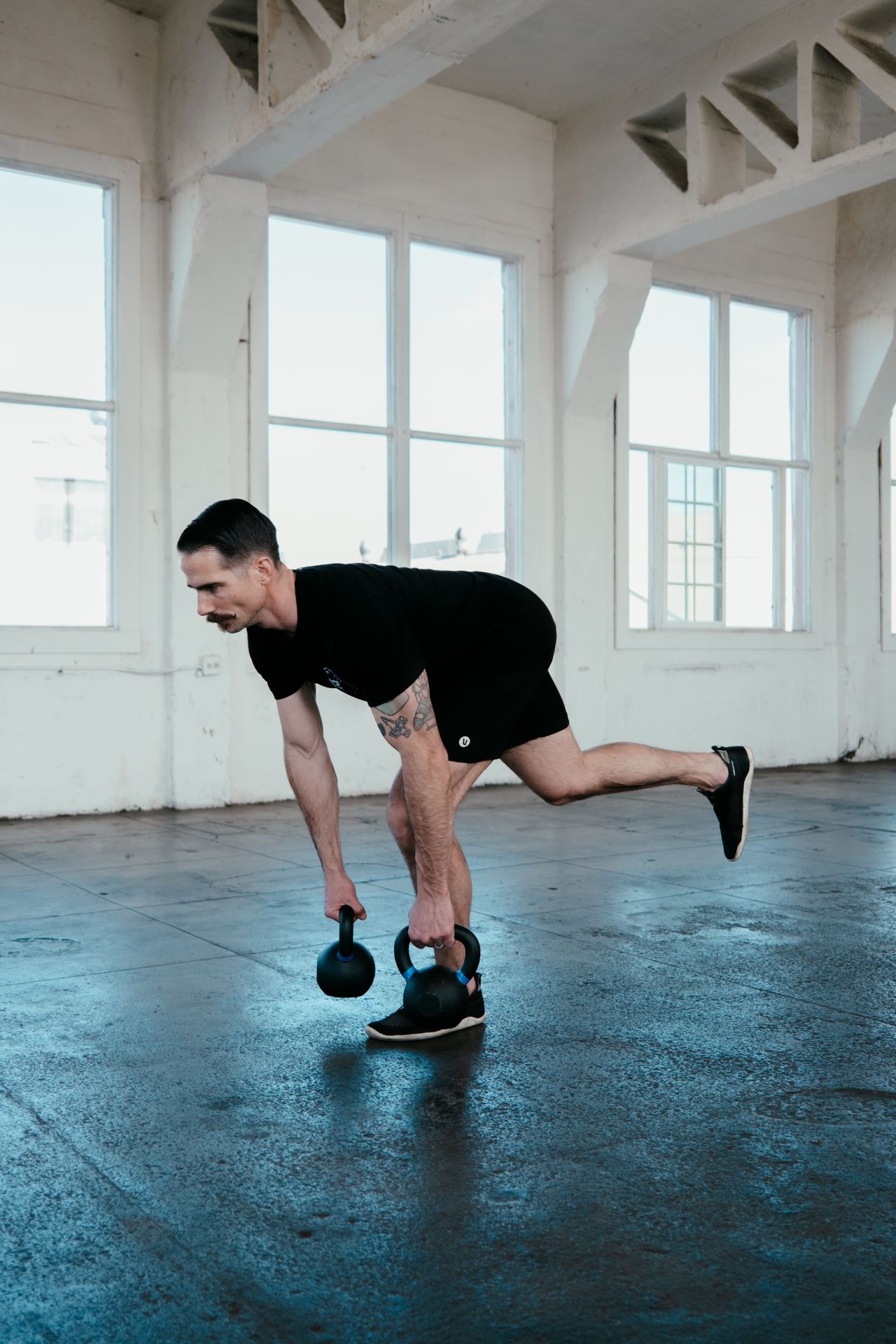 Man performing a one leg Romanian deadlift holding two kettlebells in front