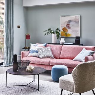 a living room with green walls, pink sofa, fluffy white armchair, blue footstool and black circular coffee table