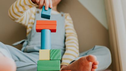 Little girl stacking colourful wooden building blocks 
