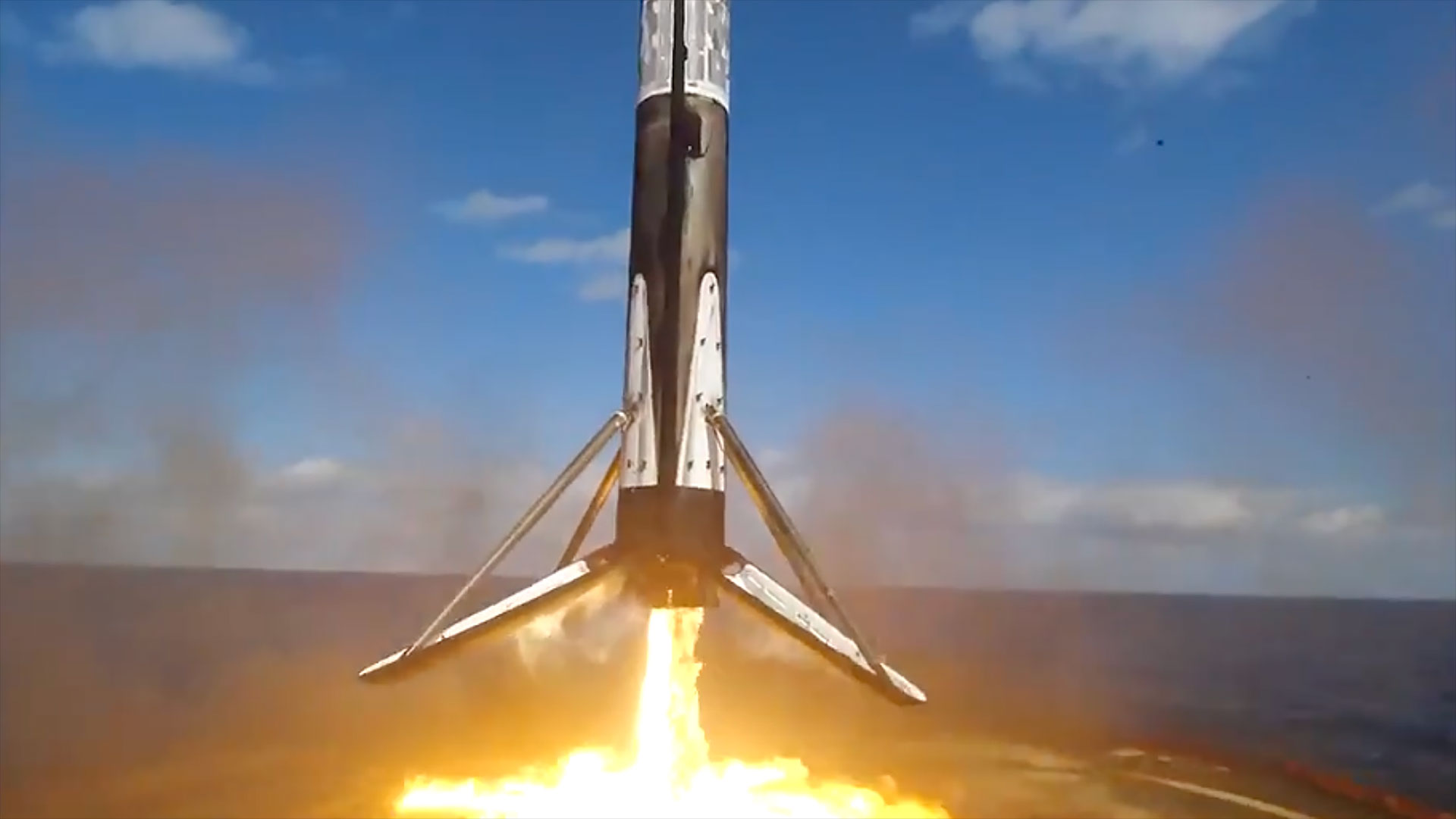 The first stage of a black and white rocket fires its engines to land on a drone ship stationed at sea