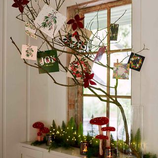 Branch decorated with Christmas cards in front of window with Christmas decorations