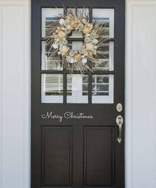 Black painted front door with wreath and christmas greeting message