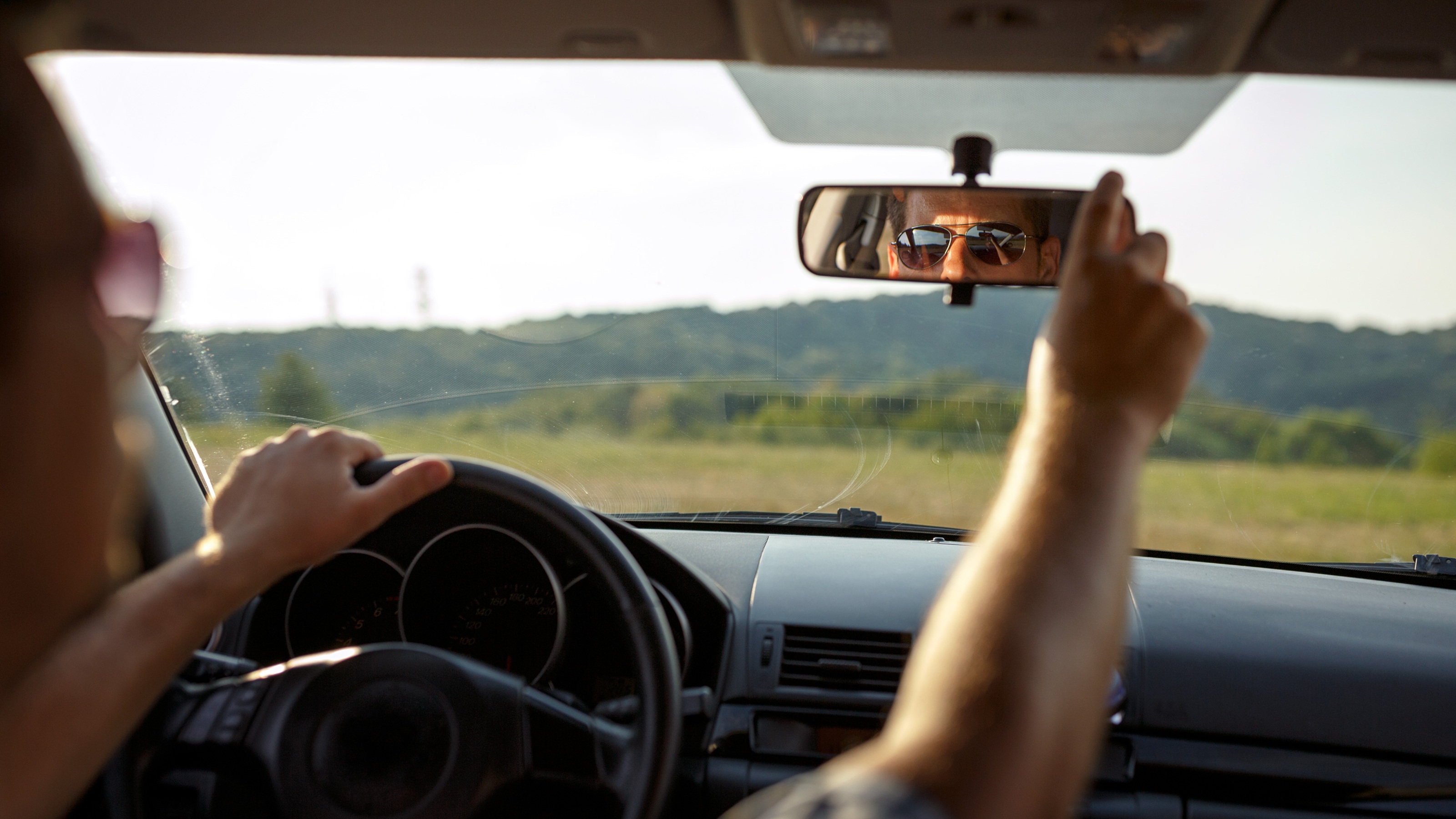 A man wearing sunglasses adjusts the rearview mirror while driving.