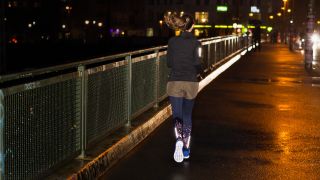 Woman running at night with reflective strips on her leggings and jacket