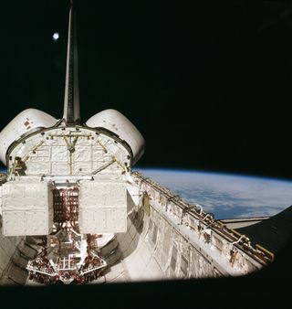 Black space and the blue and white planet Earth form the backdrop for this scene of the cargo bay and aft section of the Earth-orbiting space shuttle Columbia, photographed through the flight deck's aft windows. In the lower right corner is one of the veh