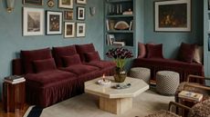Image of a limewash light blue living room with burgundy velvet seating, a gallery rail of pictures on the wall, a white marble coffee table, and a white rug with a black boarder.