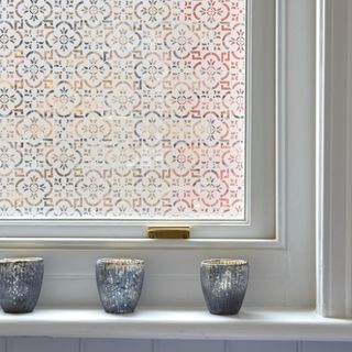A window with a patterned film and candles on the windowsill