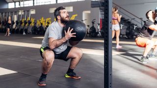 Man performing medicine ball squat throws