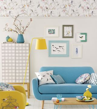 living room with a bird pattern wallpaper at the top of white walls, a yellow and blue couch and yellow floor lamp