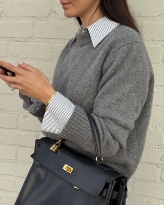 Woman wearing button-down shirt, grey sweater, and black bag.