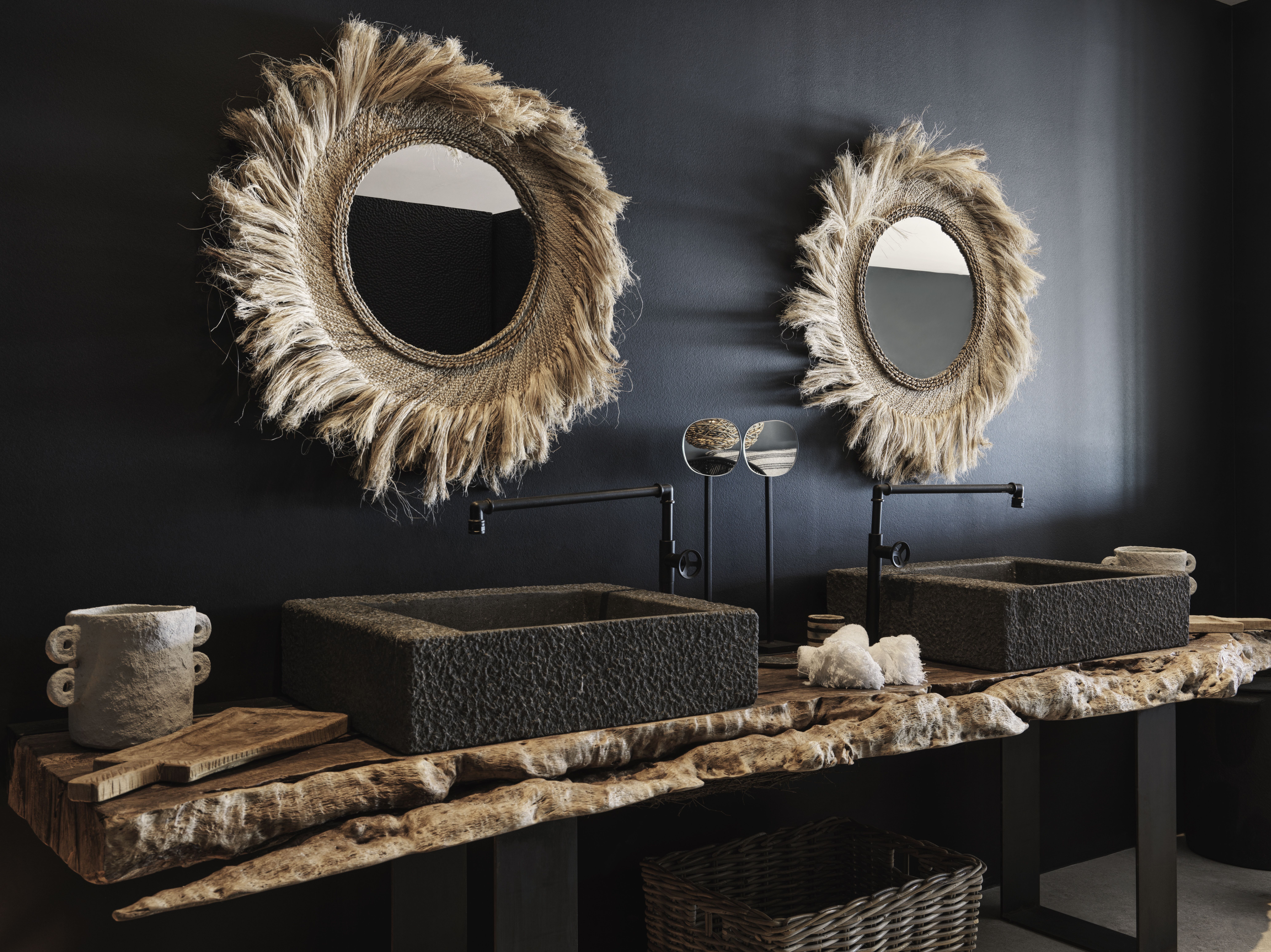A black, beige, and white-tinted hotel room filled with animal skulls, rattan mirrors, stripy sheets, and seaside views.