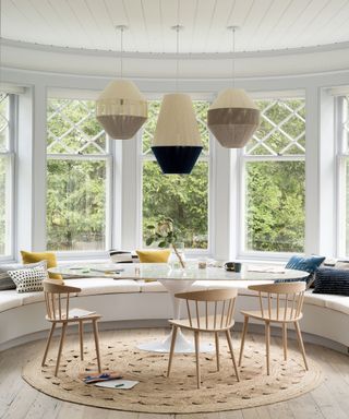 Dining area with bay window and round shapes of large glass cafe table, hessian rug and window seating with three lanterns above