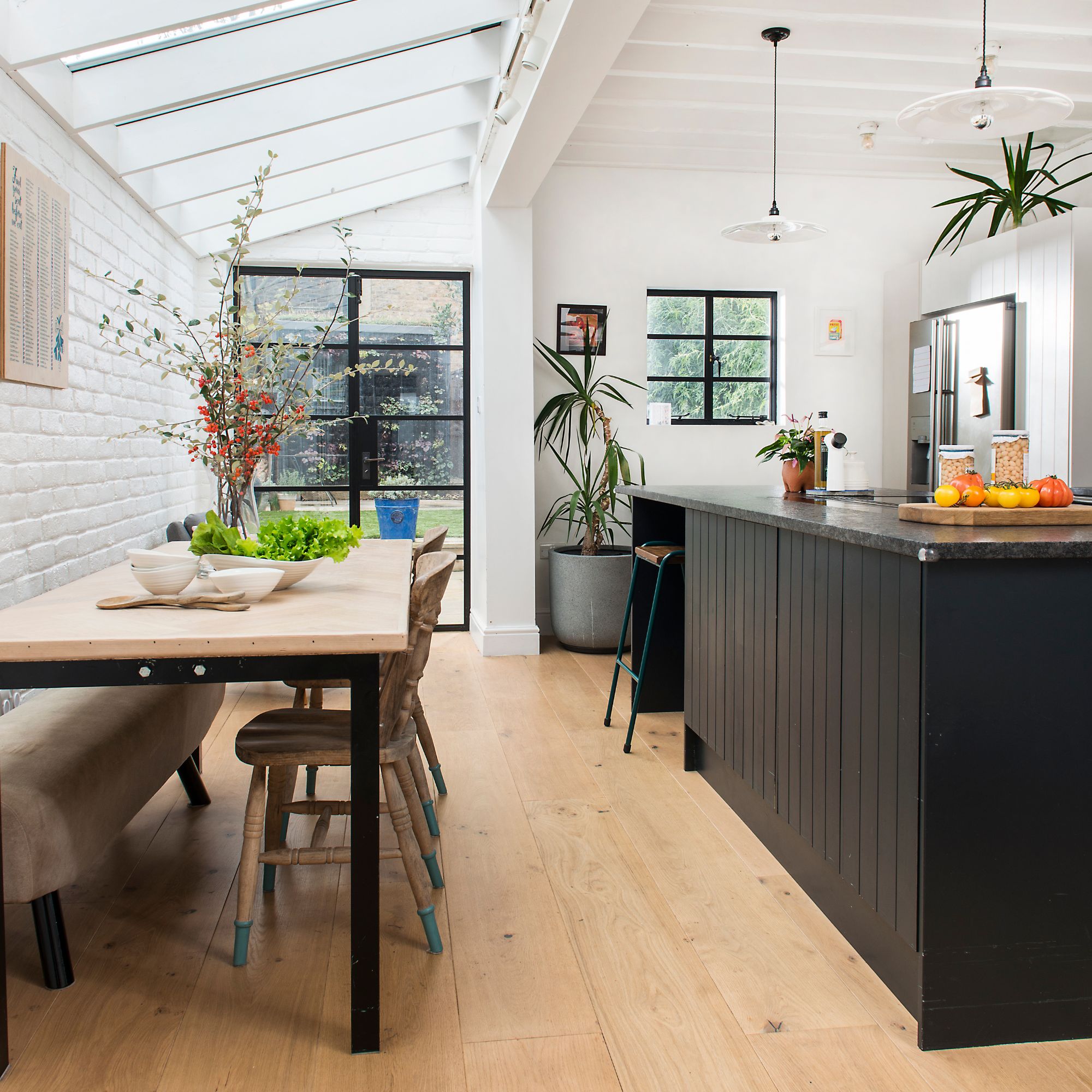 Open plan kitchen-diner with wooden floor, black wooden island and a wooden dining table and chairs