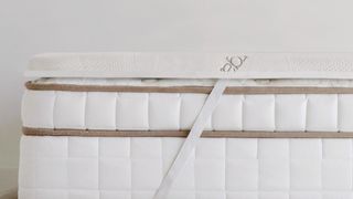 A Saatva Mattress Topper is secured via straps to the top of a Saatva mattress