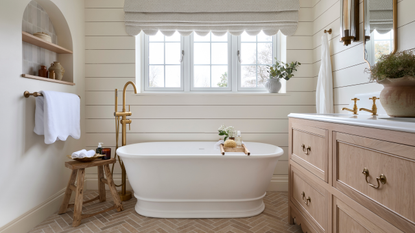 a large neutral toned bathroom with brick flooring, a freestanding white tub and scalloped hem curtains above the bath