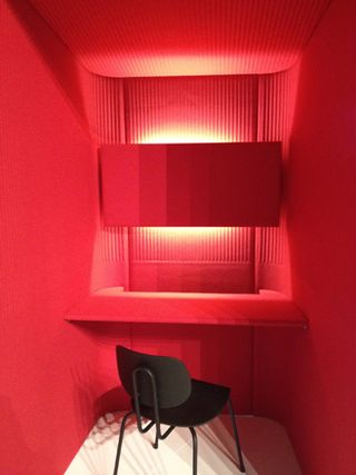 Interior image, red walls, white floor, red desk, black chair, back light shining on desk area