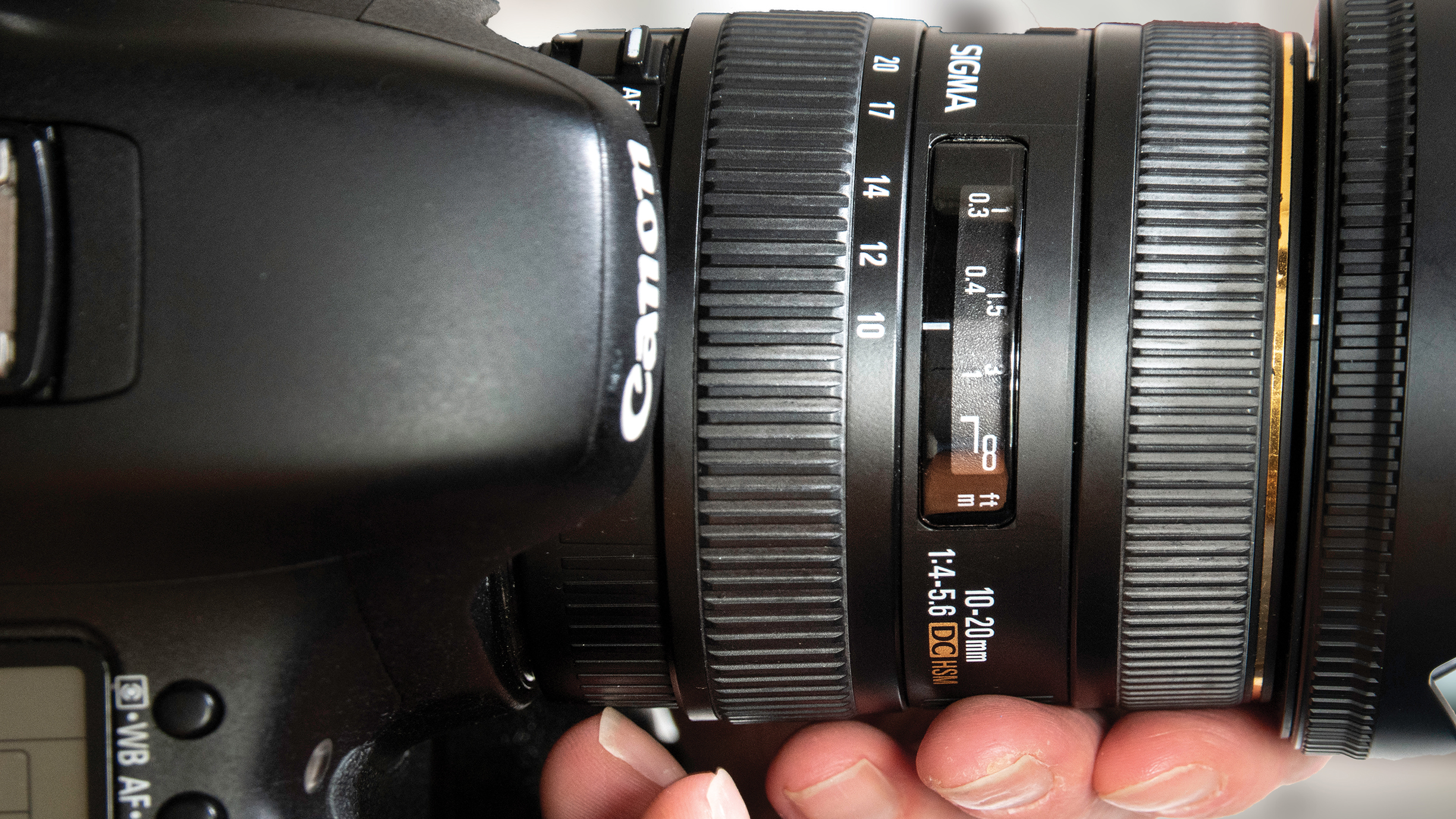 Close-up of a DSLR camera with a Sigma 10-20mm lens attached. A hand adjusts the zoom ring, indicating a focus on photography and precision