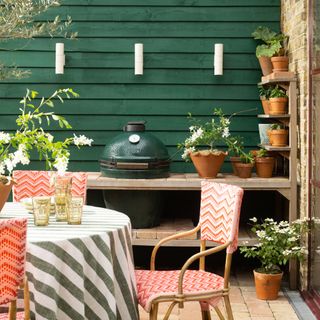 outdoor living space with green painted wall with wall lights, patterned rattan chairs, BBQ, plants, set table, tumblers