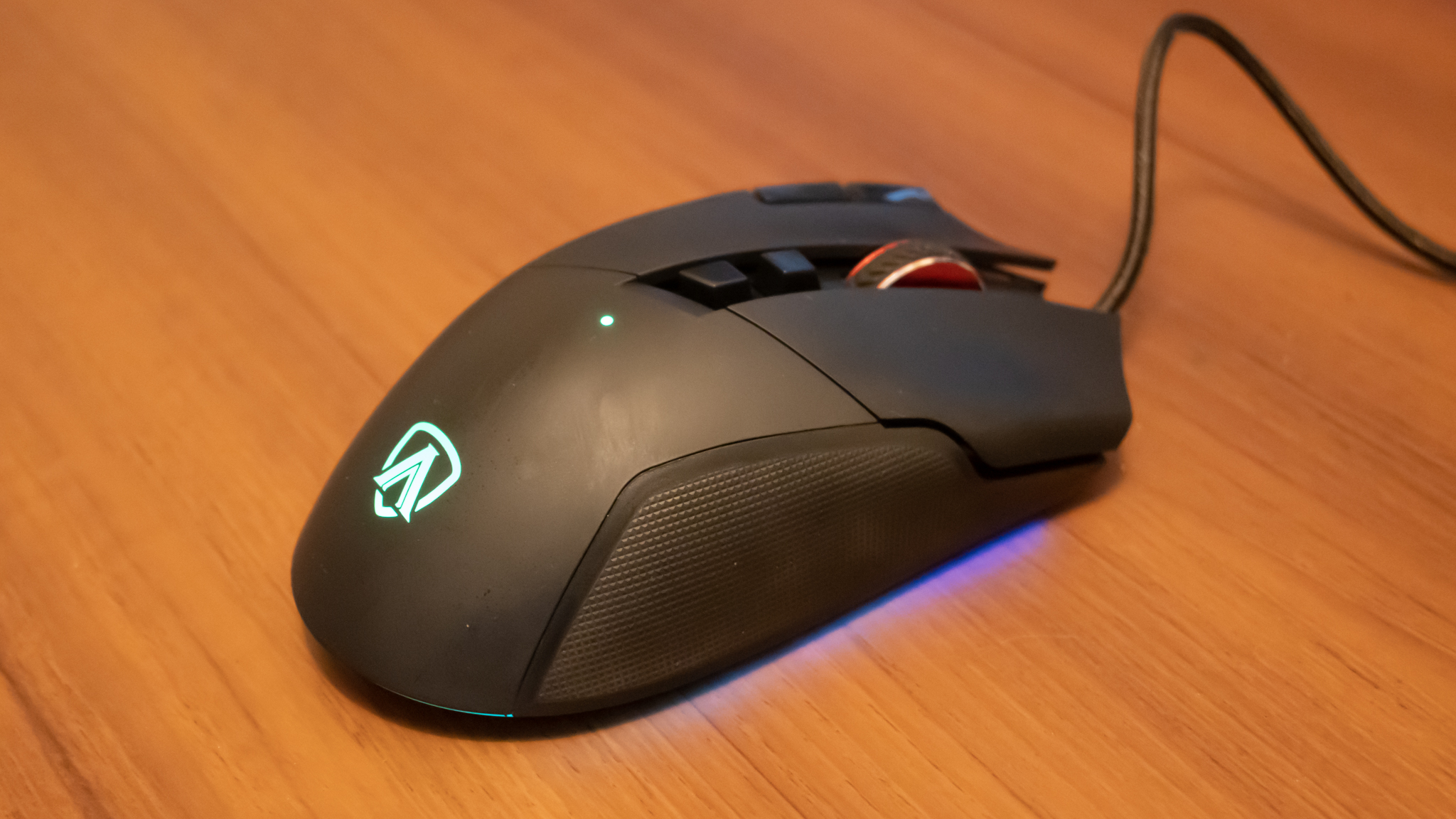 A black AOC AGON AGM600 gaming mouse sitting on a brown wooden desk