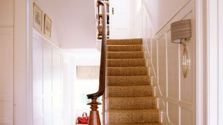 Looking up carpeted stairs with white wood panelling 