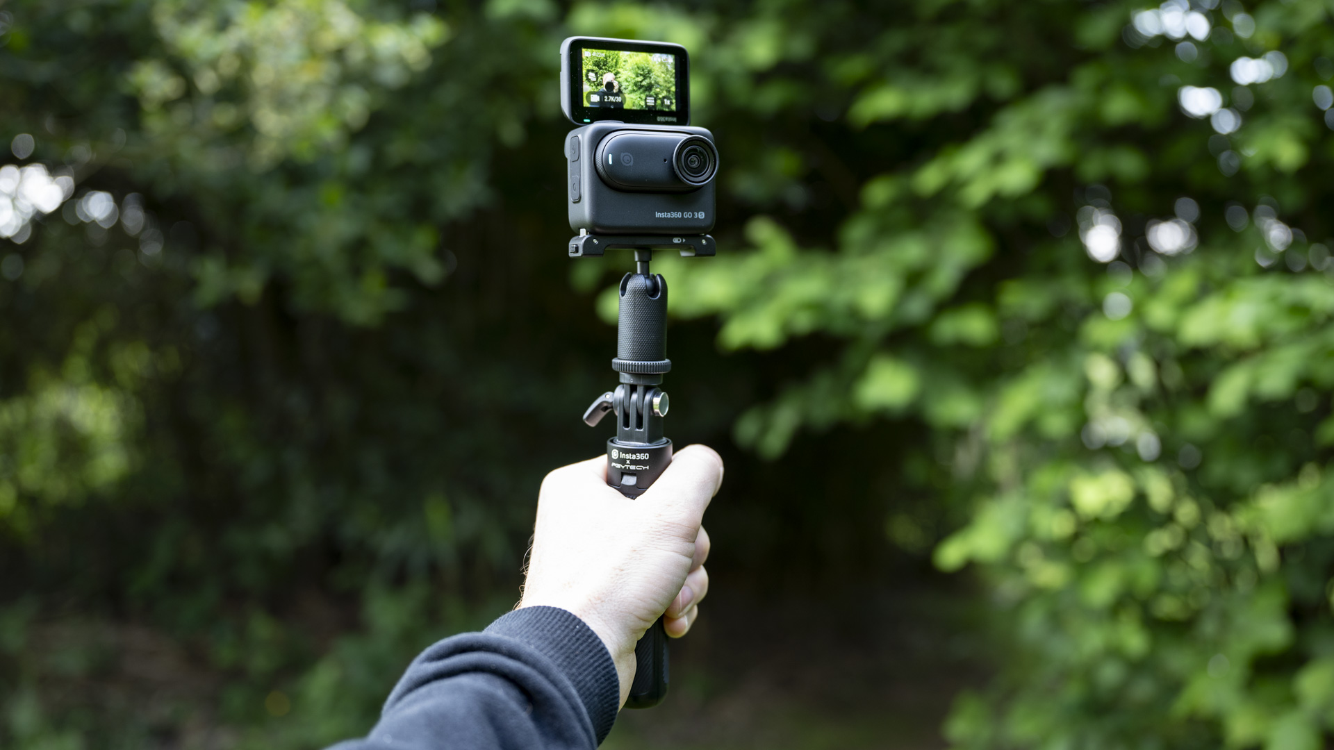 Insta360 Go 3S camera in its housing attached to a selfie stick, outdoors