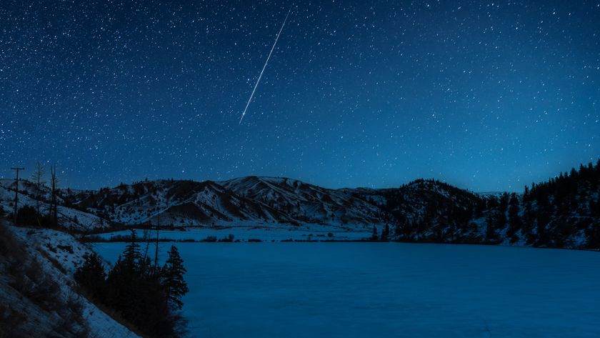 A shooting star is pictured streaking down through a starry sky above a frozen lake it night, bordered by snow-dappled hills.