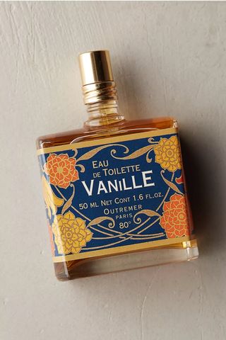 Outremer Vanille Eau De Toilette in rectangular golden bottle with large vintage-inspired blue and orange label and long golden cap on painted beige background with shadow 