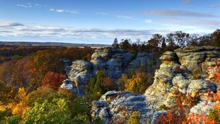 Rock formations surrounded by trees with autumnal foliage on sunny day,
