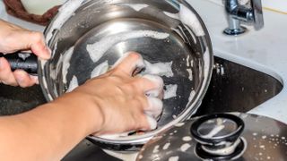 A stainless steel pan being washing with soapy water in the sink