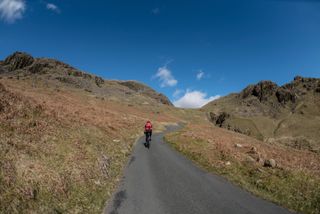 Image shows cyclist climbing Hardknott Pass in the Lake District