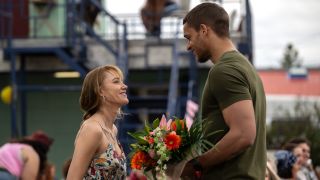 Kenna looking at Ledger who is holding flowers and looking at her.