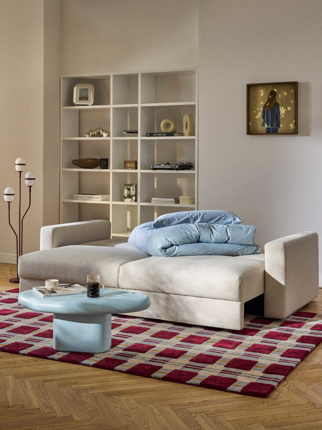 An unfolded boucl&amp;eacute; sofa bed from Westwing in a living room with a patterned rug, a blue coffee table, and a floor lamp