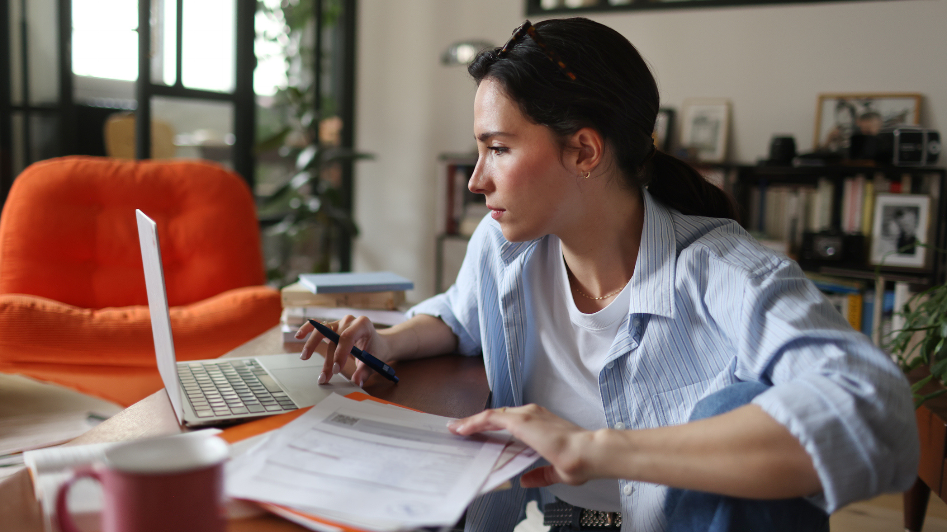 A woman on a laptop working from home, surrounded by sheets of paper