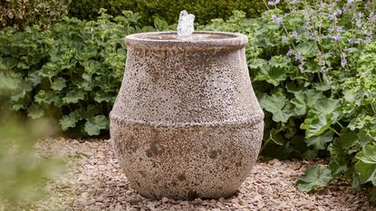 water feature pot on gravel garden with hedges around it