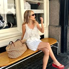 Influencer Chloe Kath Butler wears a white lace camisole and white denim shorts with red flip flops. 