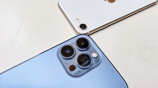 The iPhone SE and iPhone 13 Pro Max, side by side on a table, face down with their camera modules facing each other