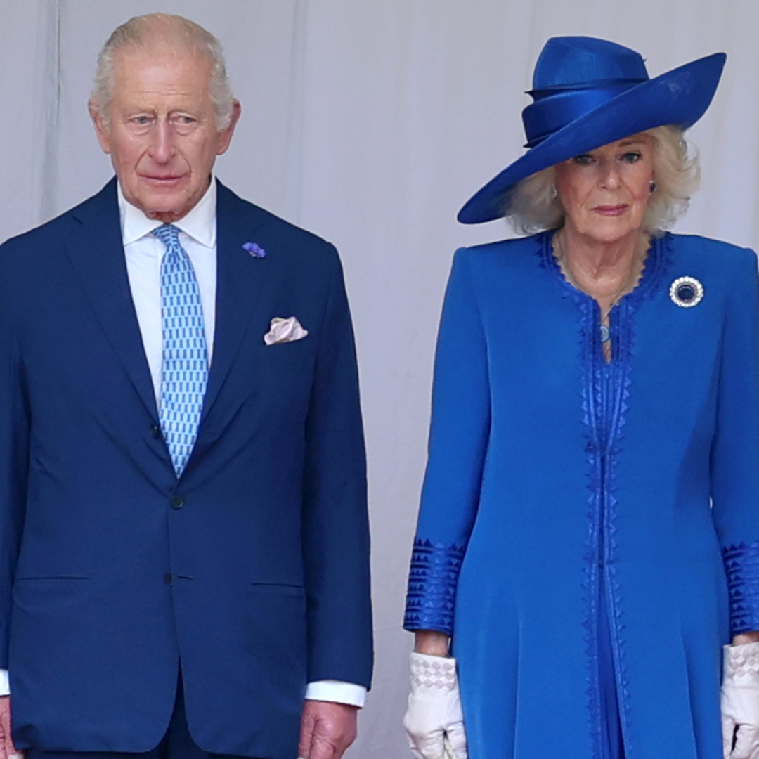 King Charles wears a navy suit with a light blue tie while Queen Camilla wears a royal blue dress with a matching hat