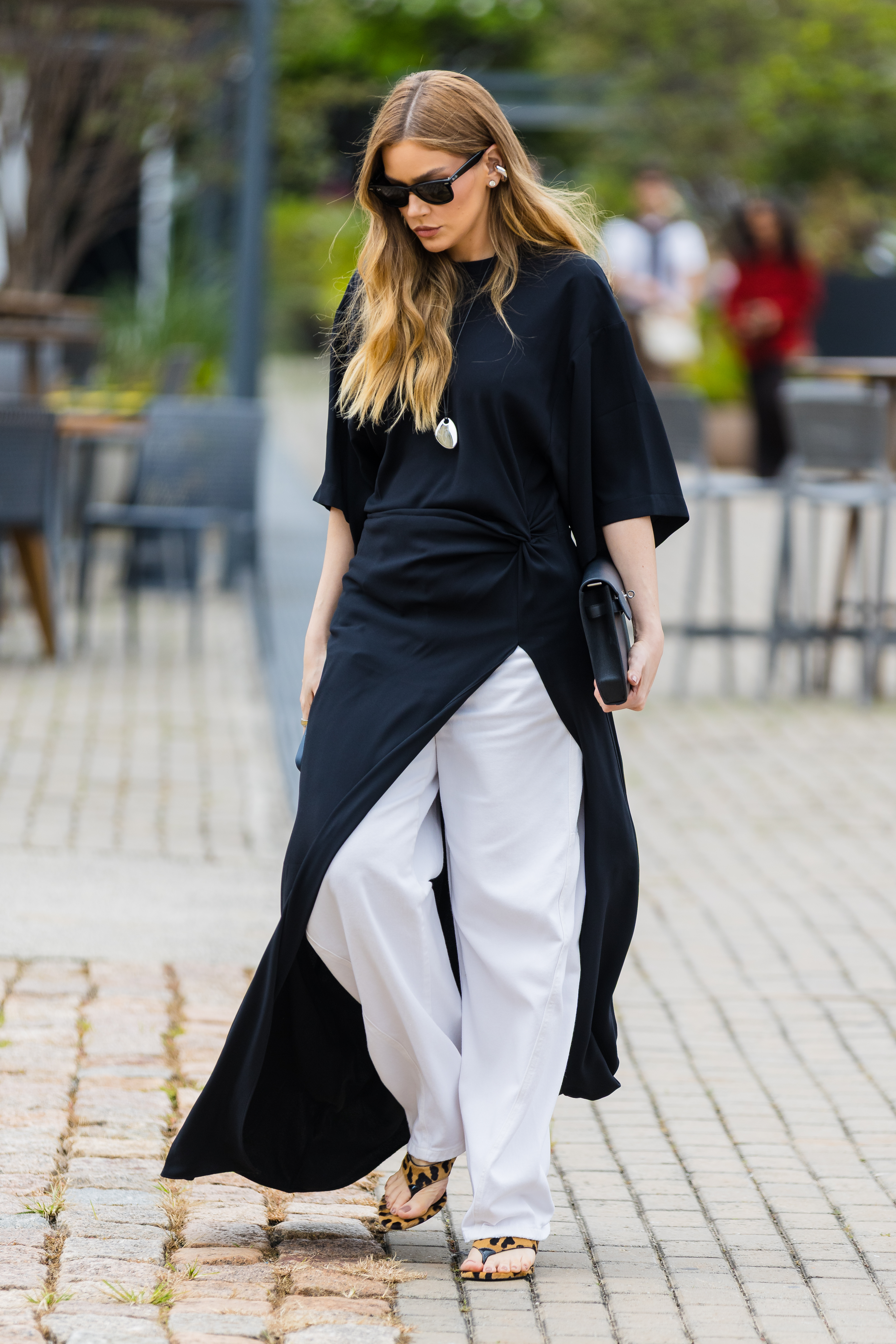 a woman wears a black maxi asymmetrical dress, white jeans, and leopard flip-flops.
