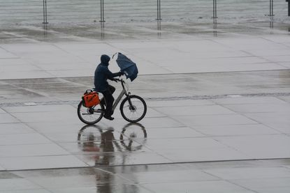 A cyclist struggles with an umbrella in the wind